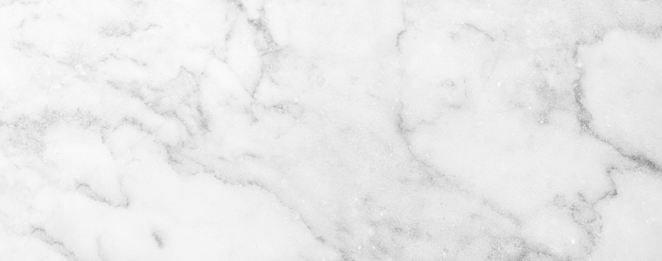 White marble surface with subtle gray veining and soft, cloudy patterns. The texture appears smooth and polished, giving a clean and elegant appearance.