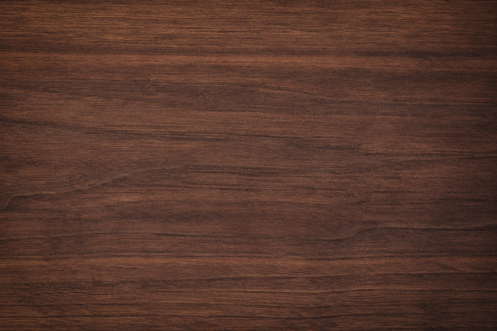 A close-up view of a smooth, dark brown wooden surface with visible grain patterns and subtle texture throughout.